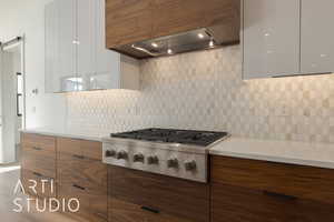 Kitchen featuring custom exhaust hood, white cabinetry, stainless steel gas stovetop, a barn door, and decorative backsplash