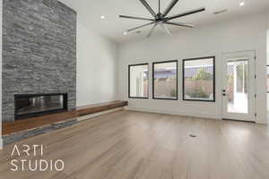 Unfurnished living room featuring ceiling fan, a stone fireplace, and light wood-type flooring