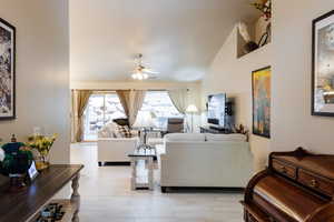 Living room with ceiling fan, high vaulted ceiling, and light wood-type flooring