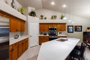 Kitchen with sink, hanging light fixtures, appliances with stainless steel finishes, a kitchen breakfast bar, and a kitchen island with sink