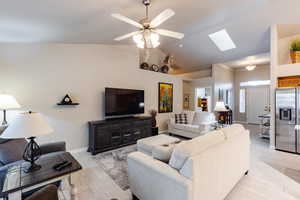 Living room featuring ceiling fan, vaulted ceiling with skylight, and light wood-type flooring