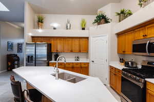 Kitchen with sink, a breakfast bar, appliances with stainless steel finishes, an island with sink, and decorative light fixtures