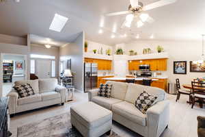 Living room featuring high vaulted ceiling, ceiling fan with notable chandelier, and light wood-type flooring