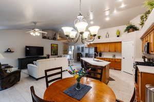 Dining space featuring vaulted ceiling, sink, ceiling fan with notable chandelier, and light hardwood / wood-style flooring