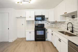 Kitchen featuring sink, white cabinetry, black appliances, decorative backsplash, and light wood-type flooring