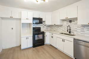 Kitchen with sink, light hardwood / wood-style flooring, white cabinetry, black appliances, and decorative backsplash