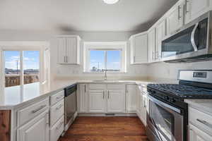 Kitchen featuring appliances with stainless steel finishes, sink, white cabinets, kitchen peninsula, and light stone countertops