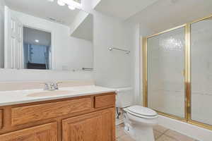 Bathroom with a shower with door, vanity, tile patterned floors, and toilet