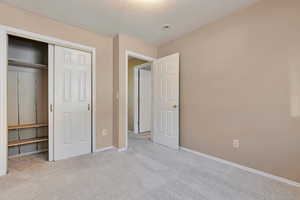 Unfurnished bedroom featuring light colored carpet, a closet, and a textured ceiling