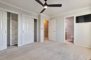 Unfurnished bedroom with ornamental molding, light carpet, two closets, and ensuite bath