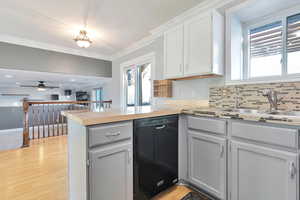 Kitchen featuring black dishwasher, sink, ornamental molding, kitchen peninsula, and light hardwood / wood-style flooring