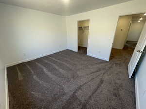 Unfurnished bedroom featuring dark colored carpet and a walk in closet