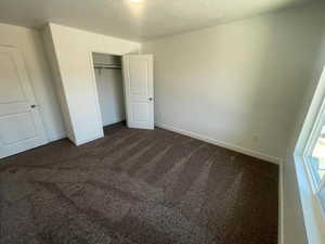 Unfurnished bedroom featuring a closet, a textured ceiling, and dark colored carpet