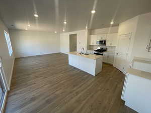 Kitchen with appliances with stainless steel finishes, dark hardwood / wood-style floors, sink, white cabinets, and a kitchen island with sink