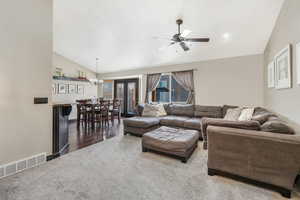 Carpeted living room featuring ceiling fan with notable chandelier and vaulted ceiling