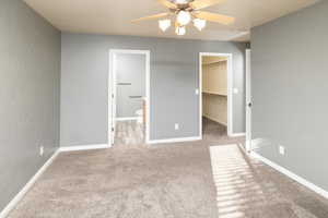 Unfurnished bedroom featuring a walk in closet, ensuite bath, light carpet, a closet, and ceiling fan