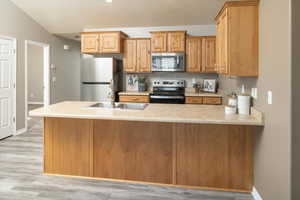 Kitchen with lofted ceiling, sink, light hardwood / wood-style flooring, appliances with stainless steel finishes, and kitchen peninsula