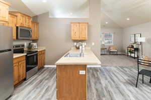 Kitchen with lofted ceiling, sink, kitchen peninsula, stainless steel appliances, and light wood-type flooring