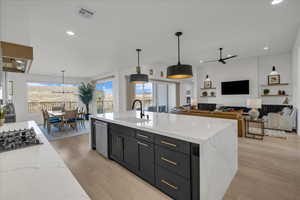 Kitchen with decorative light fixtures, light stone countertops, sink, and a center island with sink