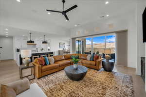 Living room with ceiling fan, sink, light wood-type flooring, and a towering ceiling