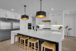 Kitchen with white cabinetry, sink, stainless steel appliances, and an island with sink