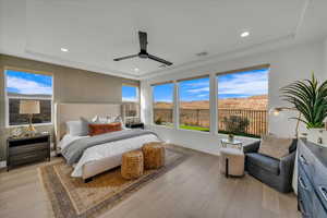 Bedroom with ceiling fan, light wood-type flooring, and a tray ceiling