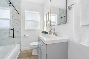 Full bathroom with vanity, tiled shower / bath, hardwood / wood-style flooring, and toilet