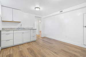 Kitchen featuring white cabinetry, light stone countertops, sink, and light hardwood / wood-style floors