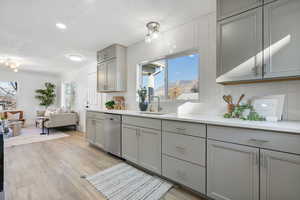 Kitchen with gray cabinets, sink, backsplash, stainless steel dishwasher, and light hardwood / wood-style floors