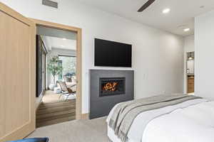 Carpeted bedroom featuring a tiled fireplace and ceiling fan