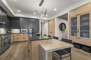 Kitchen with hanging light fixtures, range with two ovens, a center island, light brown cabinets, and light hardwood / wood-style flooring