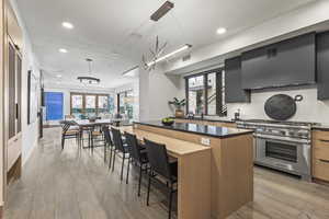 Kitchen featuring wall chimney range hood, hanging light fixtures, a center island, high end stainless steel range, and light hardwood / wood-style floors