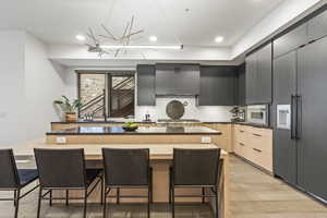 Kitchen with a breakfast bar, light hardwood / wood-style floors, a kitchen island, light brown cabinetry, and wall chimney exhaust hood