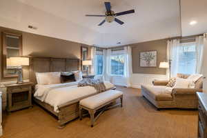 Carpeted bedroom featuring multiple windows and ceiling fan