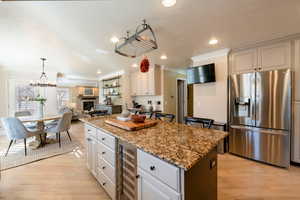 Kitchen with a kitchen island, white cabinetry, beverage cooler, light stone counters, and stainless steel refrigerator with ice dispenser