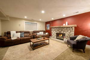 Living room with a stone fireplace, light carpet, and a textured ceiling