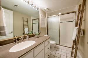 Bathroom with tile patterned floors, toilet, a textured ceiling, vanity, and a shower with door