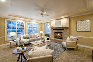 Carpeted living room with ceiling fan, ornamental molding, a raised ceiling, and a brick fireplace