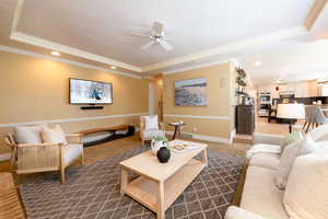 Carpeted living room featuring ceiling fan, ornamental molding, and a raised ceiling