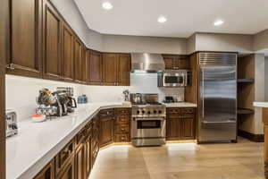 Kitchen featuring dark brown cabinetry, light hardwood / wood-style flooring, wall chimney exhaust hood, and high quality appliances