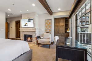 Carpeted bedroom with beamed ceiling and a stone fireplace