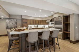 Kitchen featuring stainless steel built in refrigerator, a breakfast bar area, a large island with sink, light hardwood / wood-style floors, and wall chimney exhaust hood