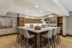 Kitchen with a large island with sink, appliances with stainless steel finishes, a kitchen breakfast bar, and wall chimney exhaust hood