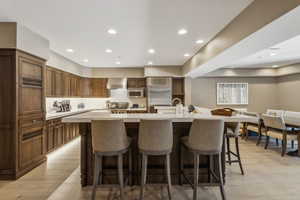 Kitchen with appliances with stainless steel finishes, a kitchen breakfast bar, wall chimney range hood, light wood-type flooring, and a spacious island