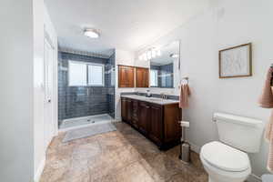 Bathroom featuring a tile shower, vanity, a textured ceiling, and toilet