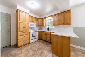 Kitchen featuring sink, tasteful backsplash, a textured ceiling, kitchen peninsula, and white appliances