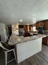 Kitchen featuring refrigerator with ice dispenser, a kitchen breakfast bar, sink, and stone counters
