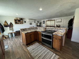 Kitchen featuring double oven range, light stone countertops, dark wood-type flooring, and a wall mounted air conditioner