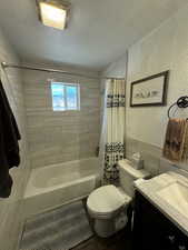 Full bathroom featuring shower / bath combo with shower curtain, vanity, toilet, and a textured ceiling