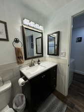 Bathroom with tile walls, hardwood / wood-style flooring, vanity, toilet, and a textured ceiling